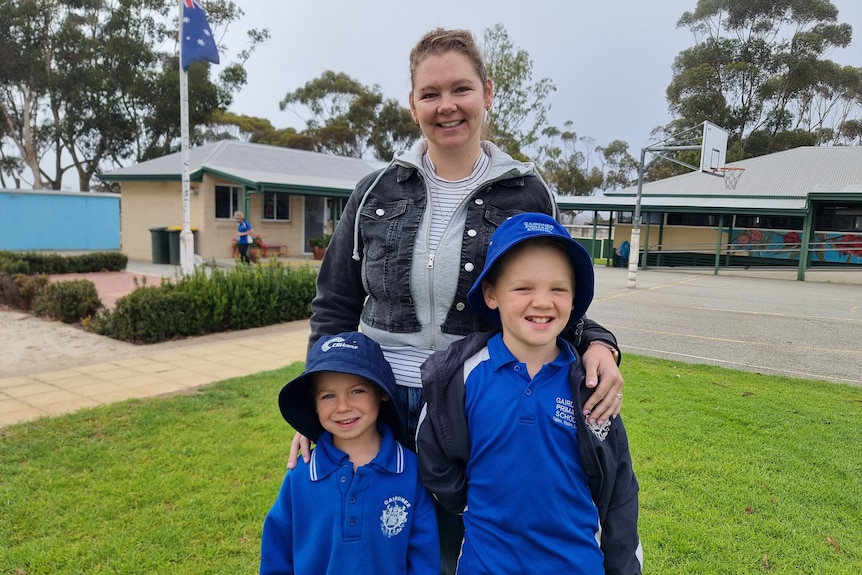 A mum with her two sons, standing in front of the school.