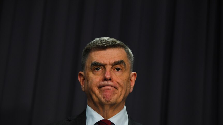 Dressed in a suit, Brendan Murphy stands in front of a dark background.