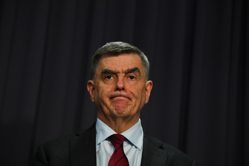 Dressed in a suit, Brendan Murphy stands in front of a dark background.