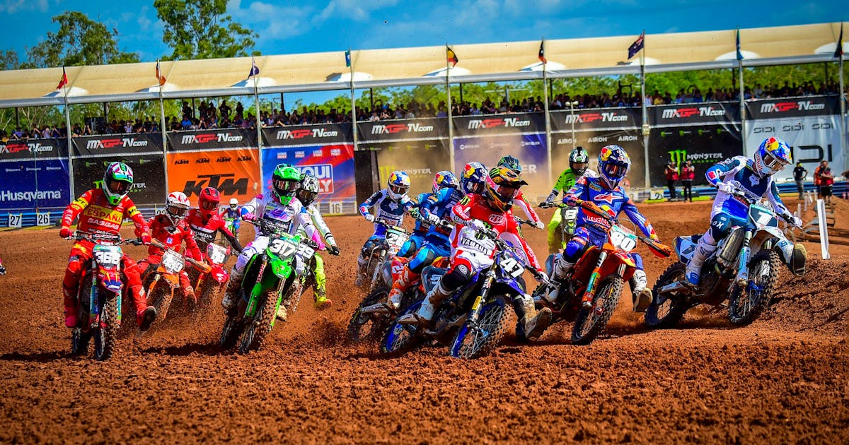 Motocross riders burst off the start gate on a red-dirt track,