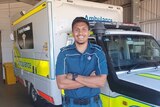 A young Indigenous man in paramedic uniform standing in front of an ambulance.