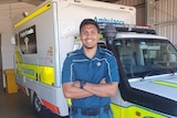 A young Indigenous man in paramedic uniform standing in front of an ambulance.