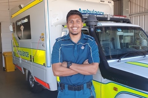 A young Indigenous man in paramedic uniform standing in front of an ambulance.