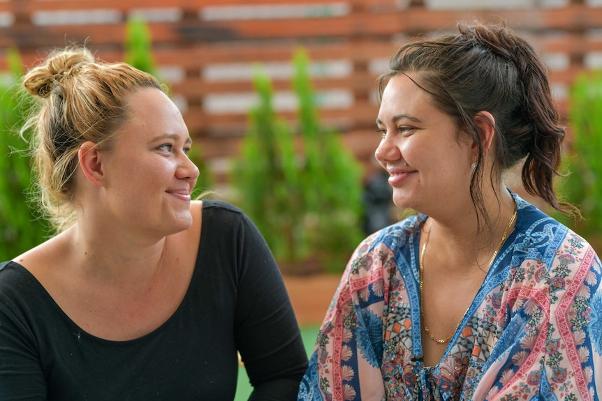 Tara and Renee smile at each other. Their hair is up in ponytails and they look happy.