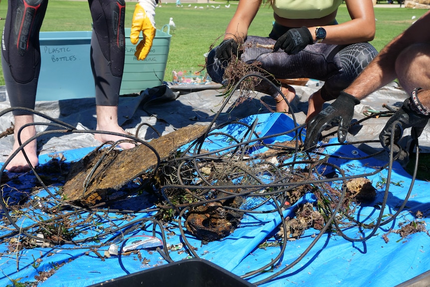 Rusted wires and other debris on a blue tarp with people in wet suit crouching.