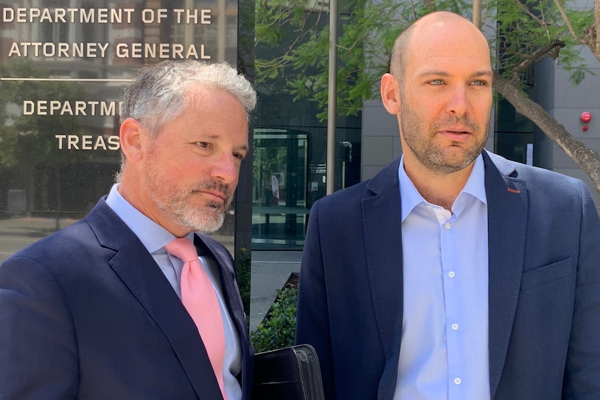 A mid-shot of two men in blue suits standing outdoors.