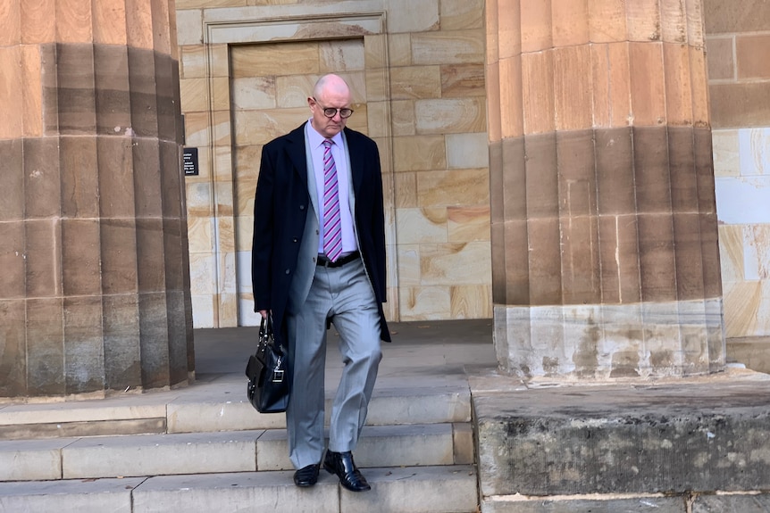 Michael Woods in a suit ad with a briefcase walks down the steps outside court