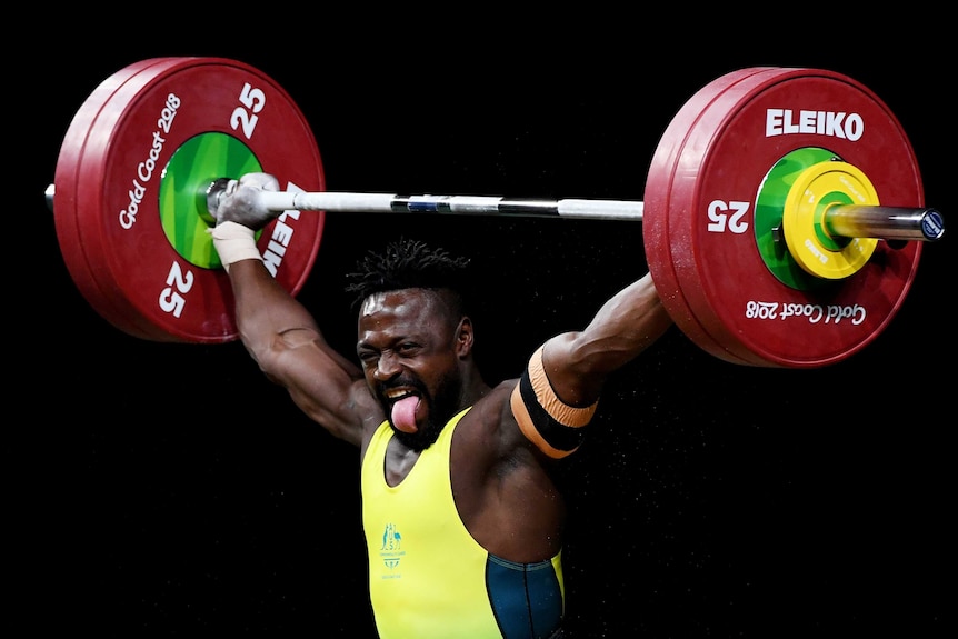Weightlifter Francois Etoundi pokes out his tongue as he holds weights above his head