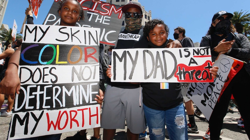 Man and two girls hold signs denouncing racism against black people