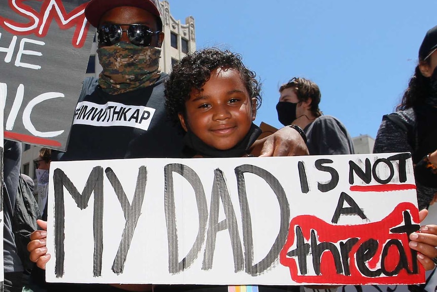 Man and two girls hold signs denouncing racism against black people