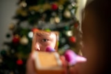 A young girl applies powder makeup in front of a Christmas tree.