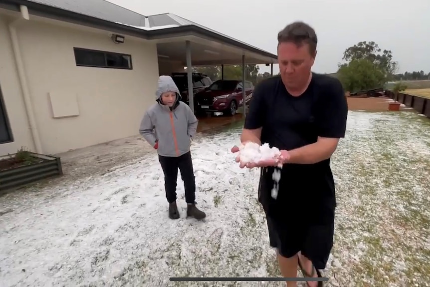 man holds a two handfuls of hail, standing on ground covered in hail