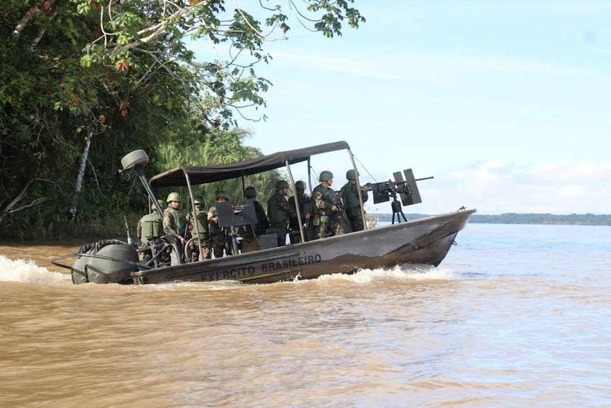 a boat with a gun mounted on the front travels along a dirty river with men in uniform and body armour aboard it