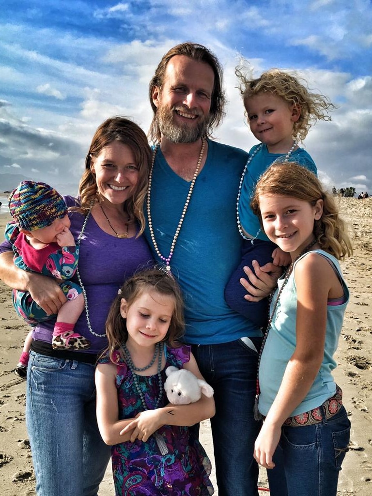 A man surrounded by three children and a woman on a beach 