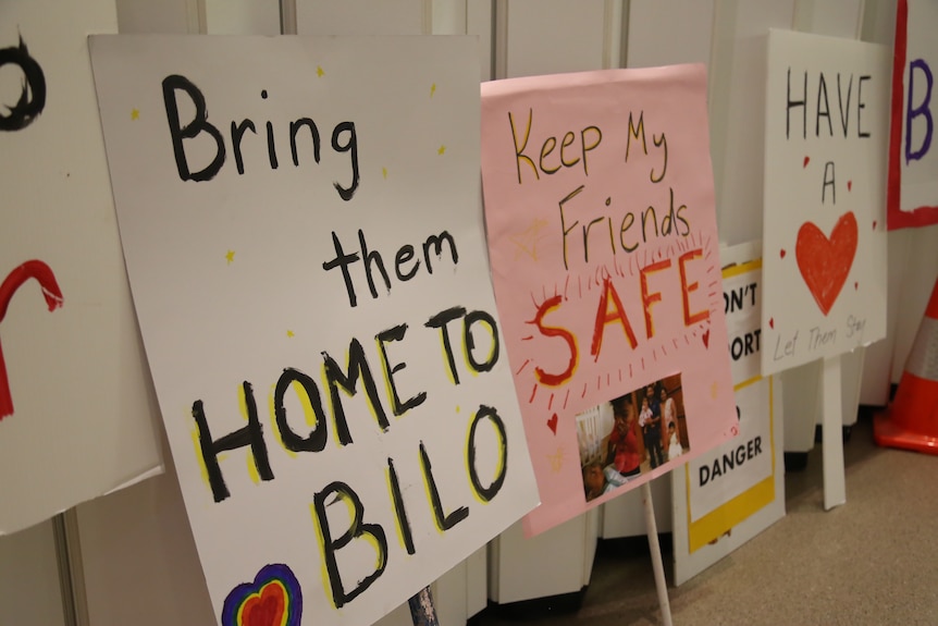 A number of Home to Bilo campaign signs in an art gallery read Bring them home to Bilo, Keep my friends safe, have a heart.