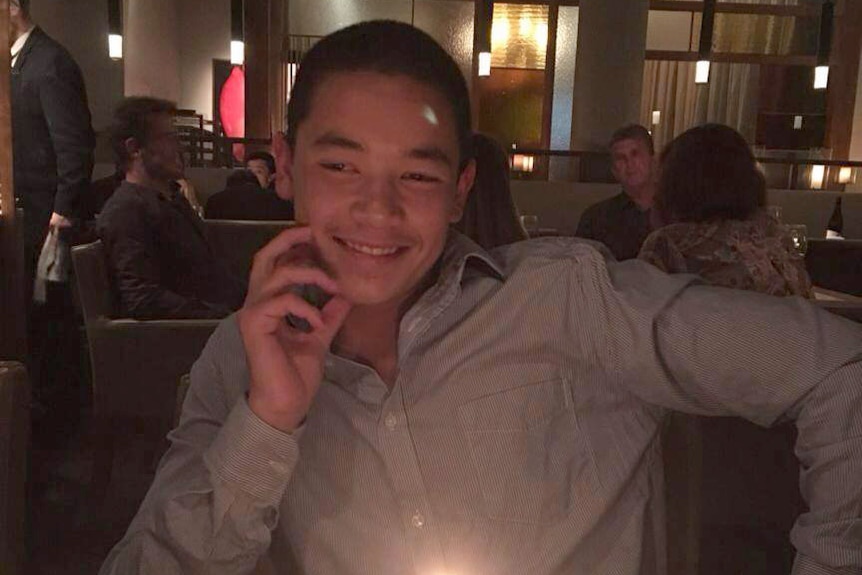 Wesley Ballantine smiles sitting at a table with a cupcake with a candle on it in front of him.