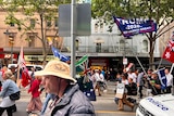 Protesters march through the Melbourne CBD holding flags and signs