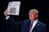 Trump smiling and holding aloft a copy of The Washington Post with the headline "Trump acquitted" on it.