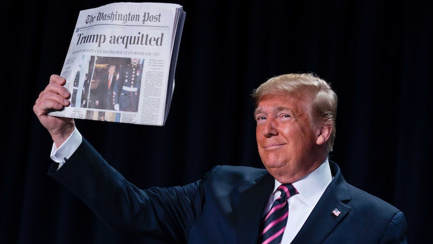 Trump smiling and holding aloft a copy of The Washington Post with the headline "Trump acquitted" on it.