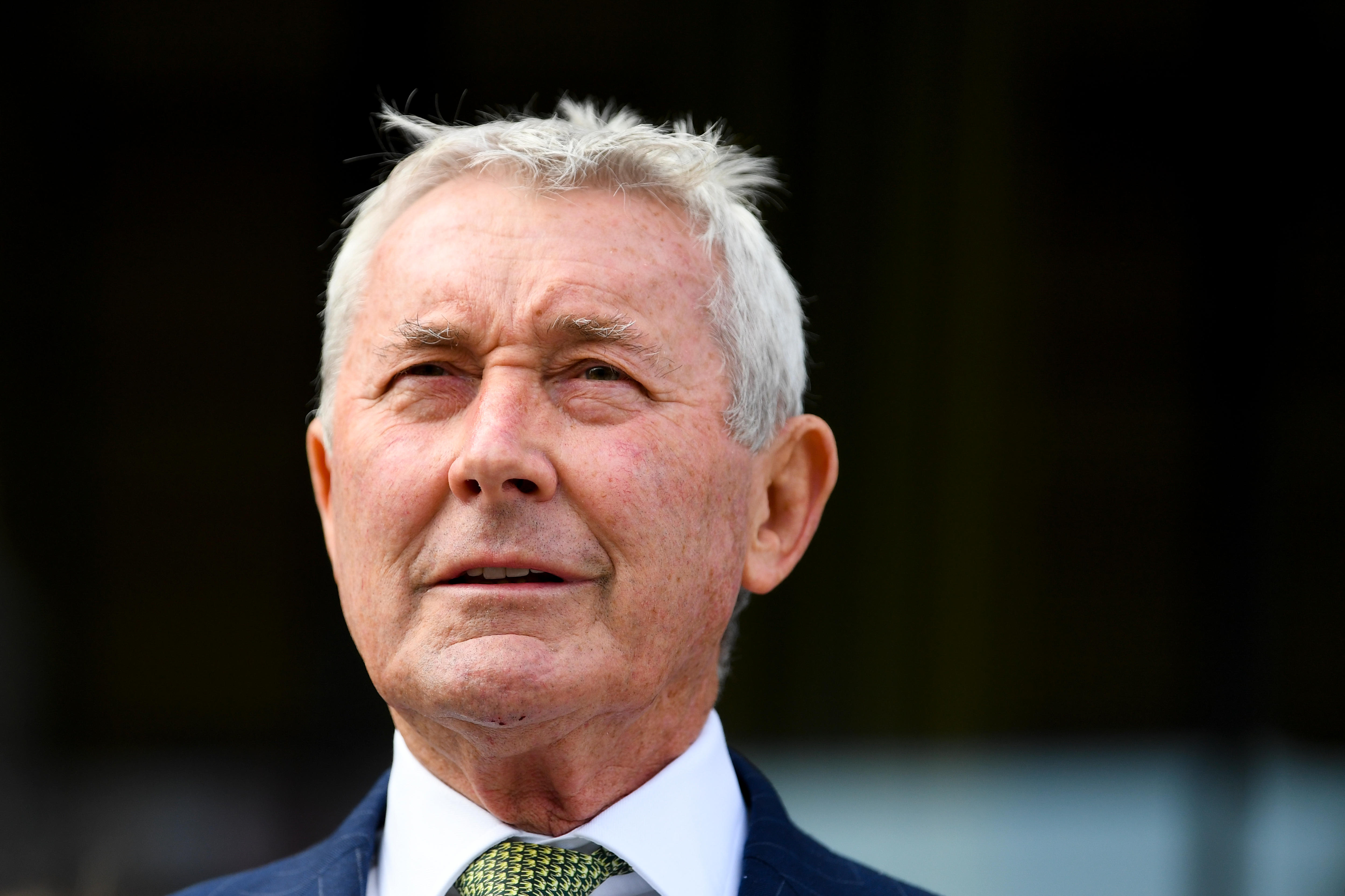 A close shot of a man wearing a suit and tie against a black background.