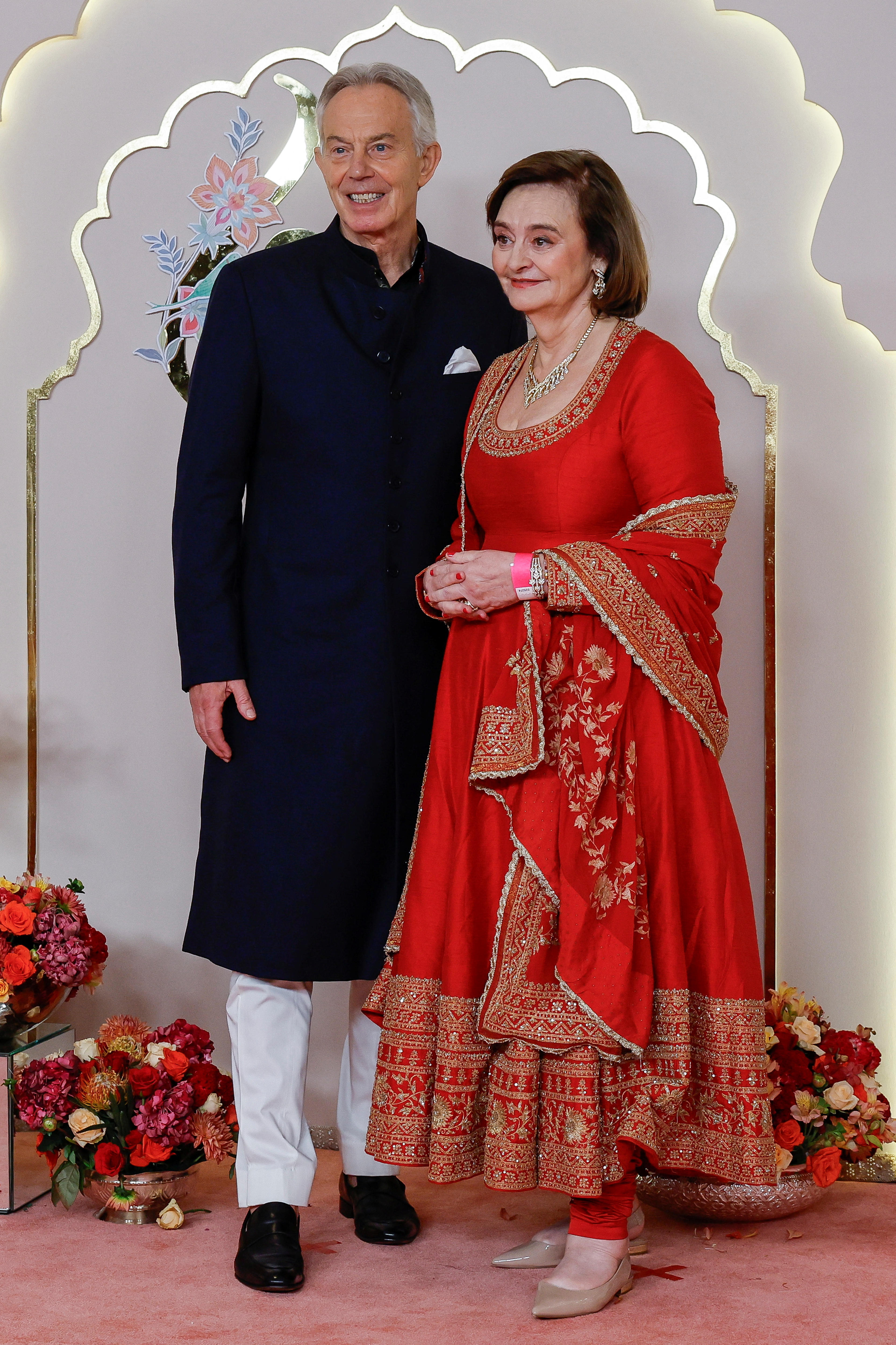 Tony Blair wears a long black tunic over white pants, while Cherie Blair wears a red ankle-length gown with a matching shawl 