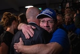 A man in a supporters cap tears up as he embraces Frydenberg