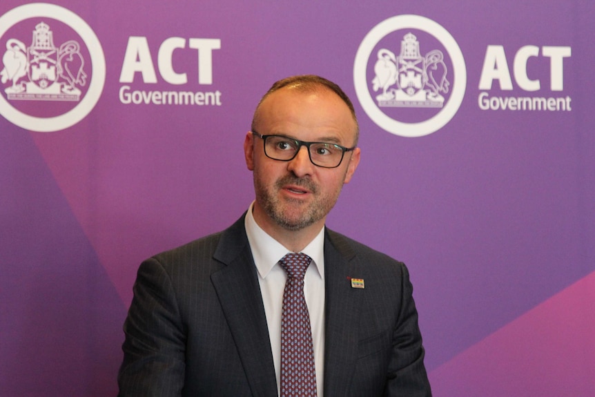 Andrew speaks in front of an ACT Government banner, wearing suit and tie.