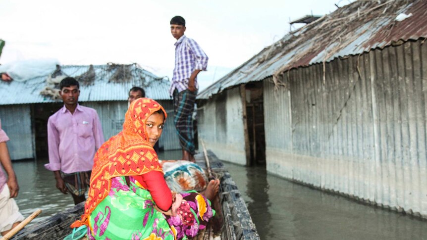 Bangladeshi villagers stand in boats and water around homes