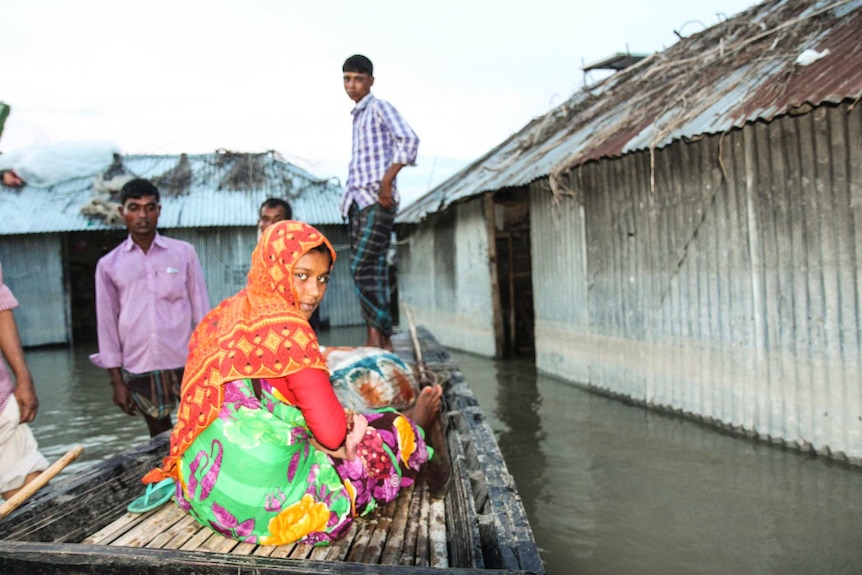 Bangladeshi villagers stand in boats and water around homes