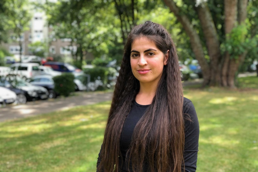 Ekhlas, a young Yazidi woman, sitting smiling in a park.