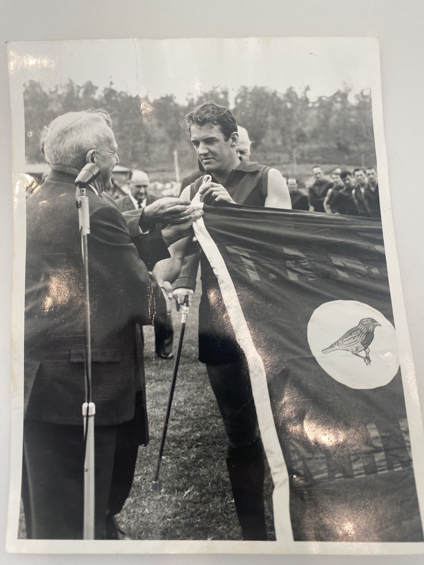 black and white photo of man in AFL gear holding a flag with another older gentleman