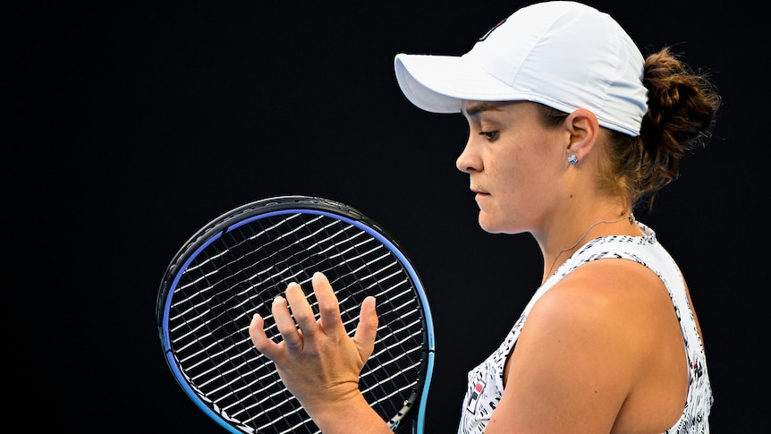 An Australian female tennis player checks the strings on her racquet.