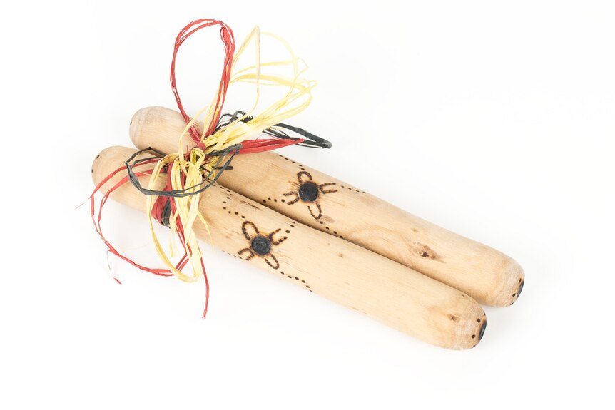 Two wooden sticks with carvings, tied up in red yellow and black twine