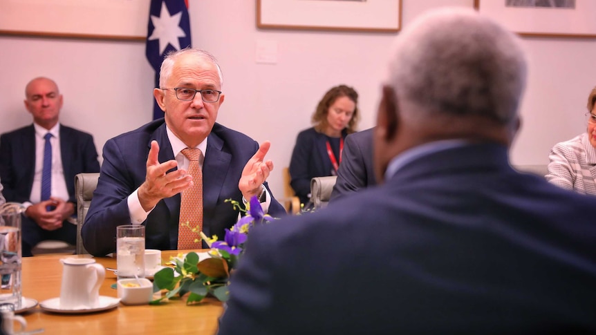 Rick Houenipwela is shot from behind in the foreground. In focus in the background is Malcolm Turnbull, gesturing with his hands