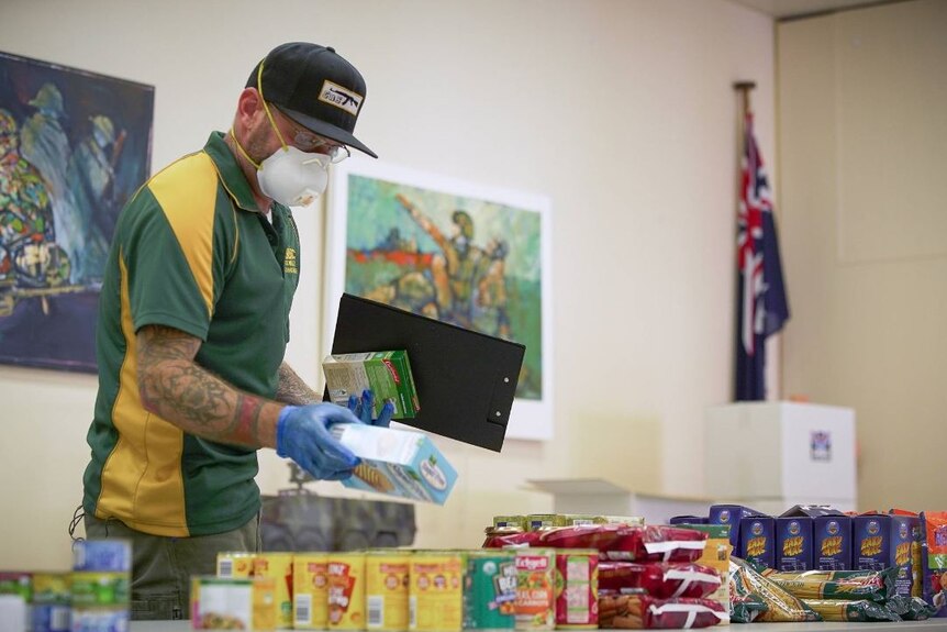 Dion Cowdray wearing a  green shirt, black cap and white face mask, sorting through food items
