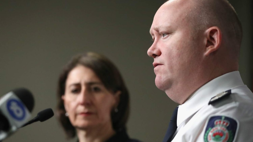 A man speaks to journalists, as a woman looks on.