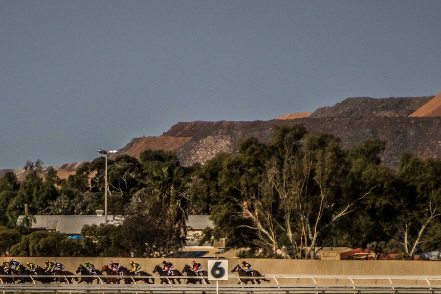 Horses round the bend at the Kalgoorlie-Boulder Racing Club, with the Super Pit gold mine visible in the background.