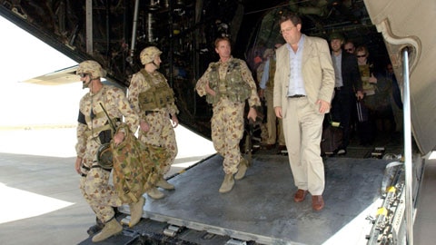 Alexander Downer wears a tan suit as he exits aircraft next to three soldiers in camouflage uniforms.