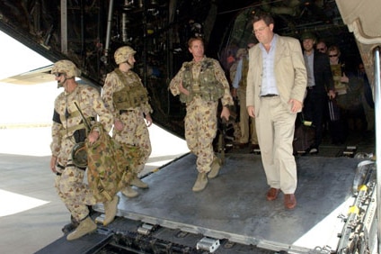 Alexander Downer wears a tan suit as he exits aircraft next to three soldiers in camouflage uniforms.