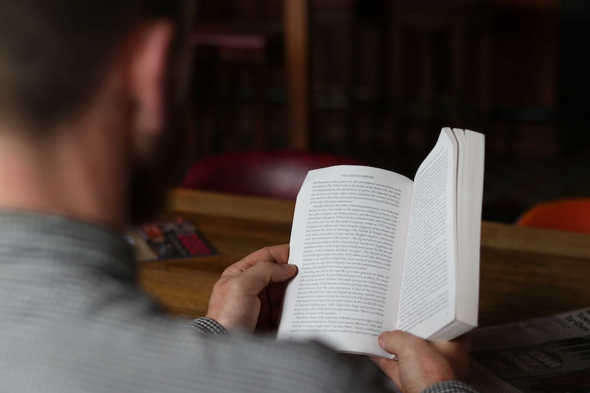 A man in silhouette reading a book at a table in the library.