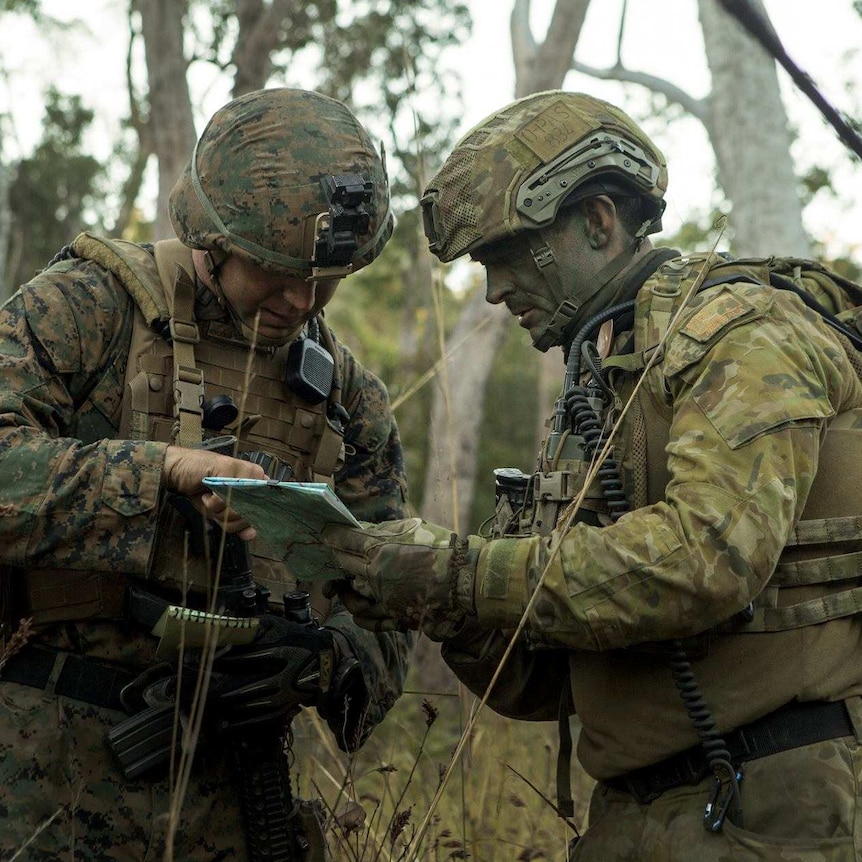 An Australian and an American soldier look at a map while out bush.