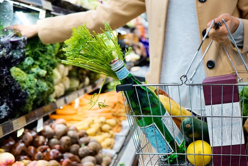 A person shopping at Australian grocery store, with a basket full of sparkling water, fruits and vegetables.