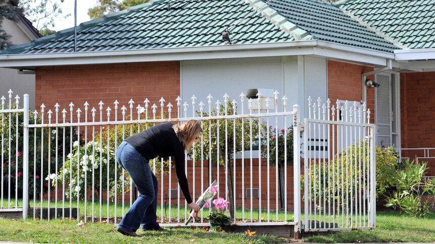 A woman places flowers at the scene of a murder of two young sisters at a house in Watsonia.