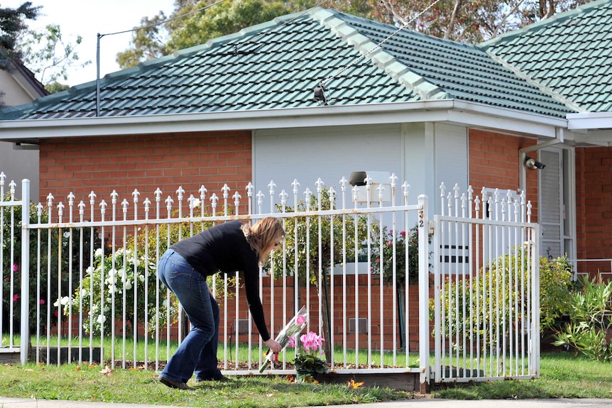 A woman places flowers at the scene of a murder of two young sisters at a house in Watsonia.
