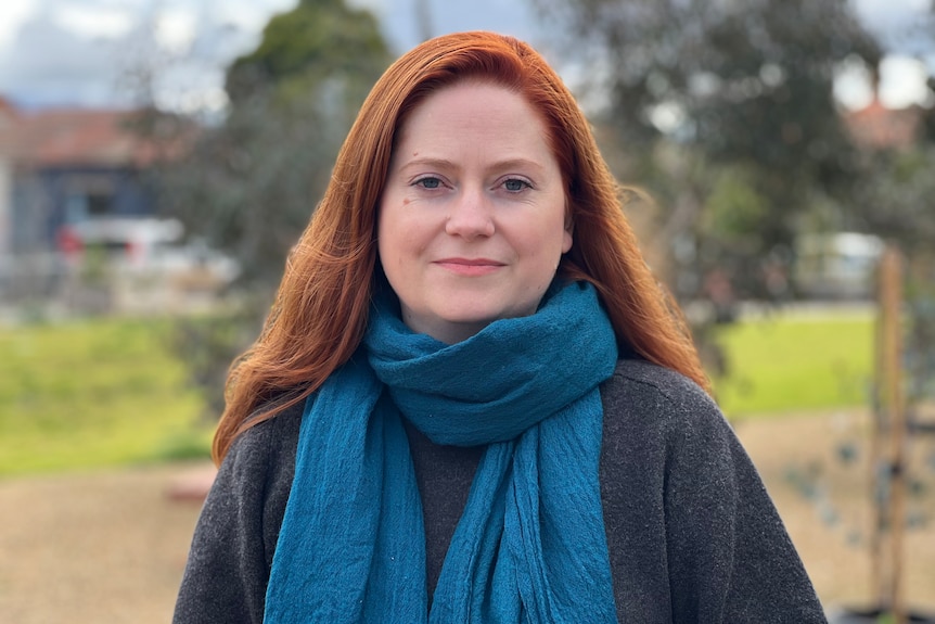 A woman with red hair looks at the camera wearing a blue scarf