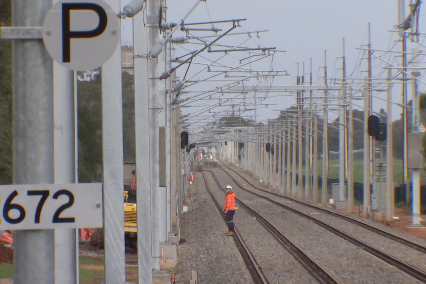 A man stands on a railway track with gantries above him