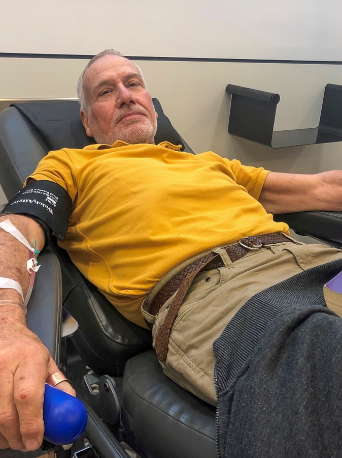 An older man in a yellow t-shirt lying back in a chair giving blood.