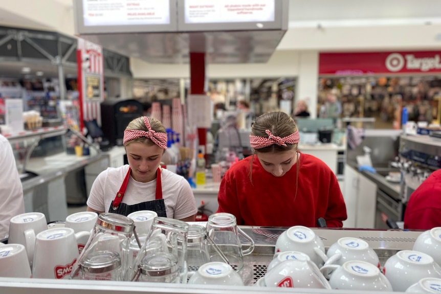 Two young women with their heads down working in an ice cream shop.