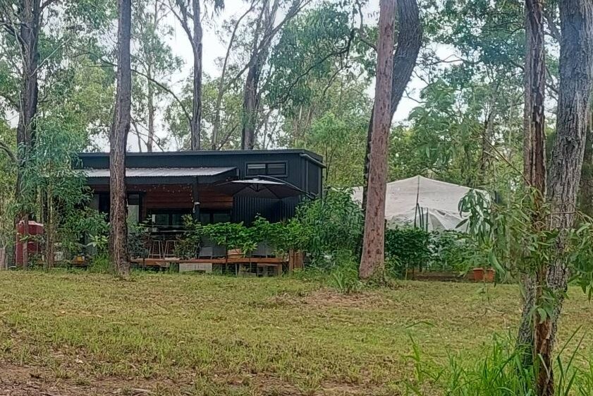 Black tiny house surrounded by trees and green paddock.