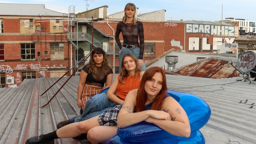 Four women sit and stand around a blue inflatable couch on a rooftop